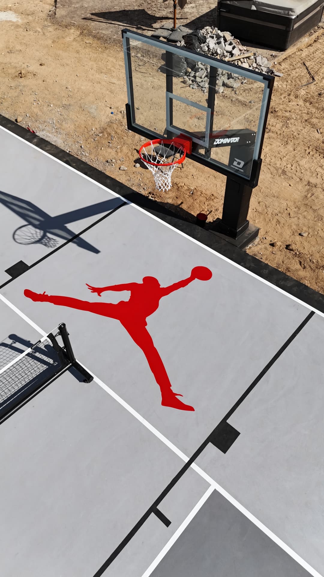 Gray backyard basketball court with custom painted logo and hoop