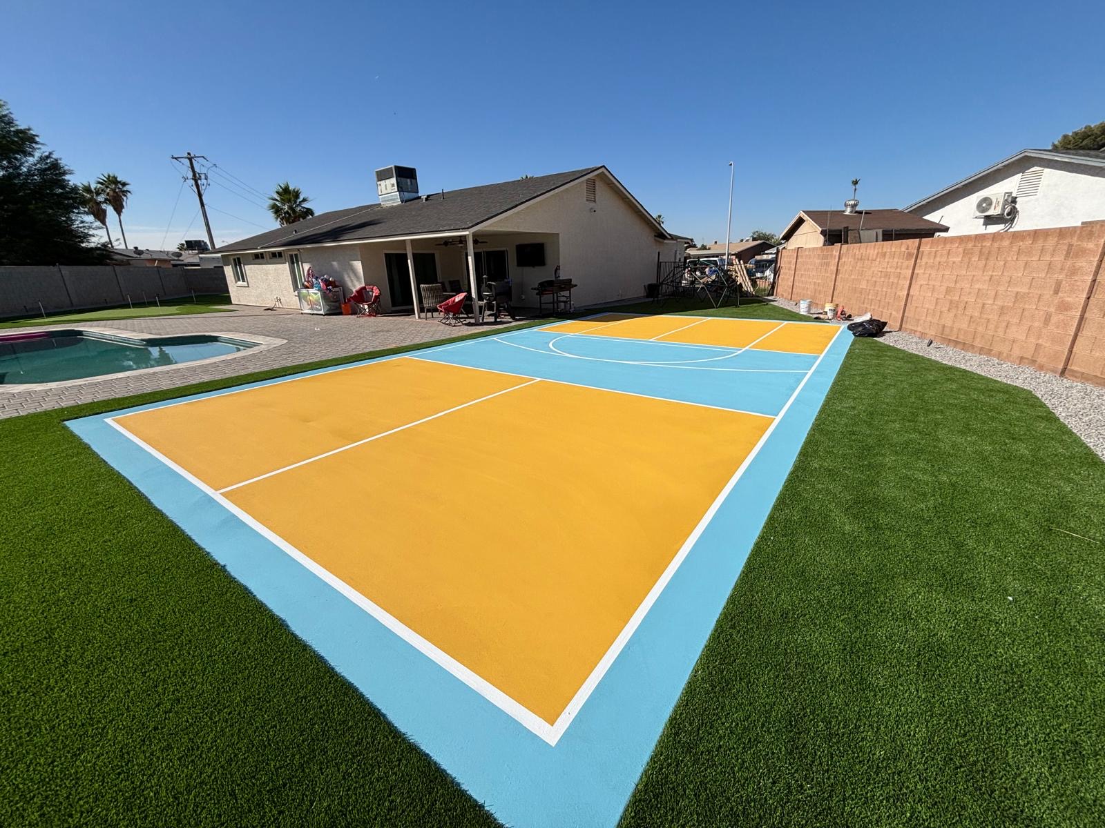 Yellow and light blue backyard basketball court next to a pool